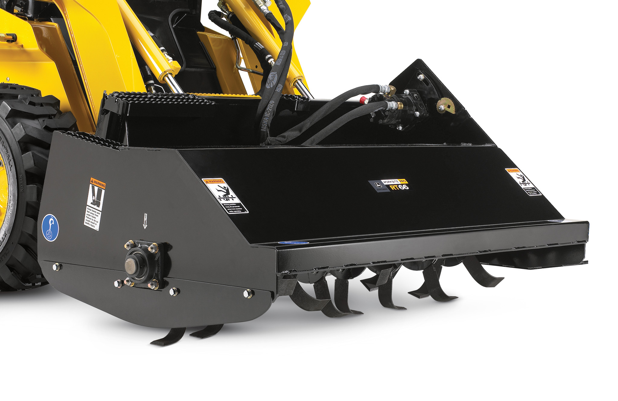 Close-up of a rotary tiller attachment with a black metal housing and curved tines along the bottom, connected to the hydraulic arms and hoses of a skid steer