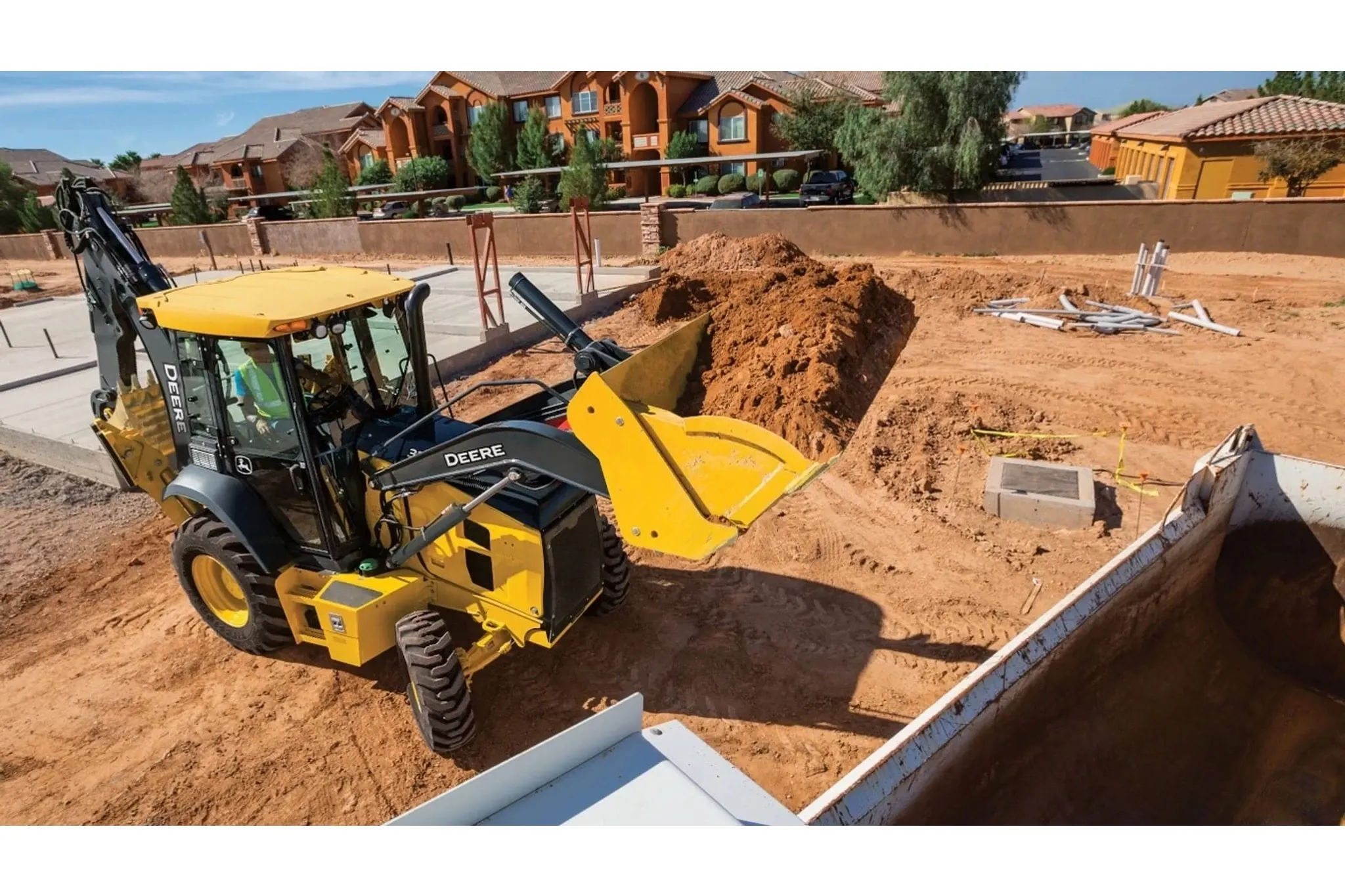 310 G-Tier Backhoe Loader loading dirt into a dump truck in a construction site