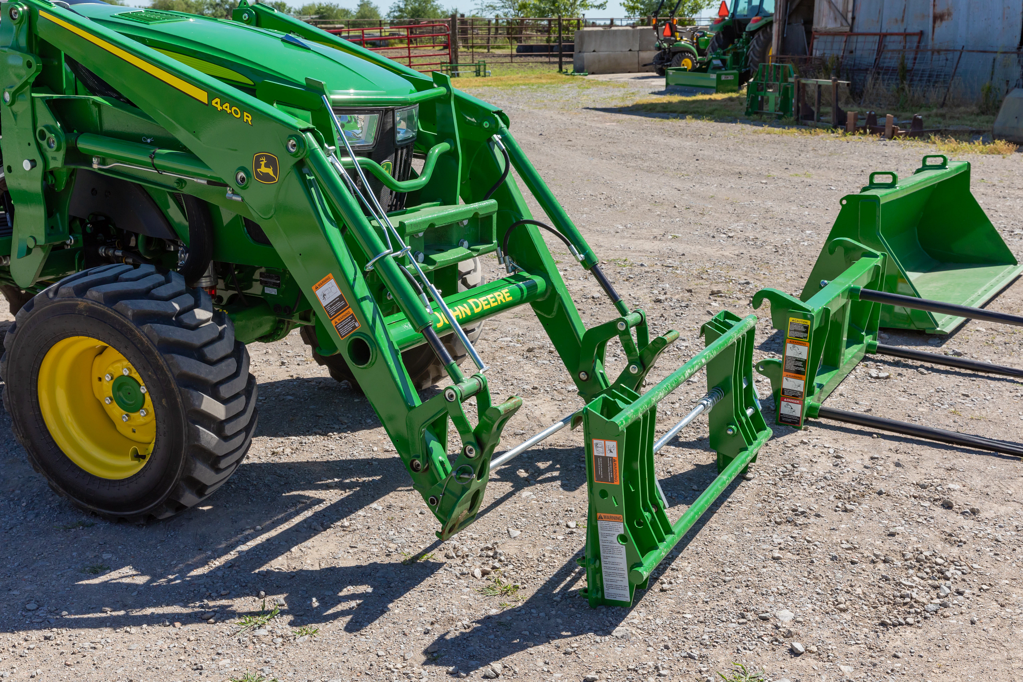 Side right view of the front of a 440R Tractor with the global carrier adapter and three frontier front-end attachments lined up in a yard