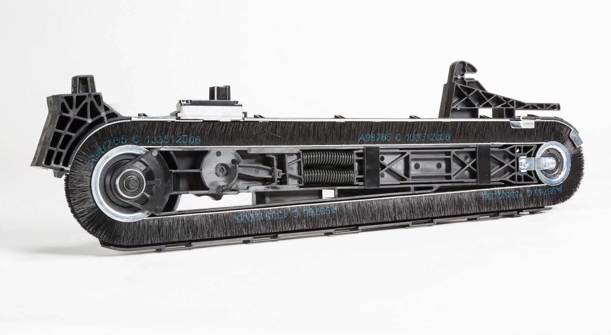 Close-up of a black industrial brush belt assembly with rotating wheels, tension spring, and dense bristles.