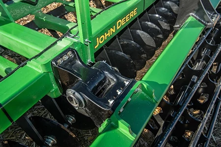 Close-up of a green high speed disk showing a black pivoting frame connection and ribbed rolling basket used for soil conditioning
