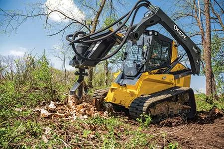 Front left view of a 333G compact track loader in a lightly-wooded area decimating a stump with a SS30 Stump shredder