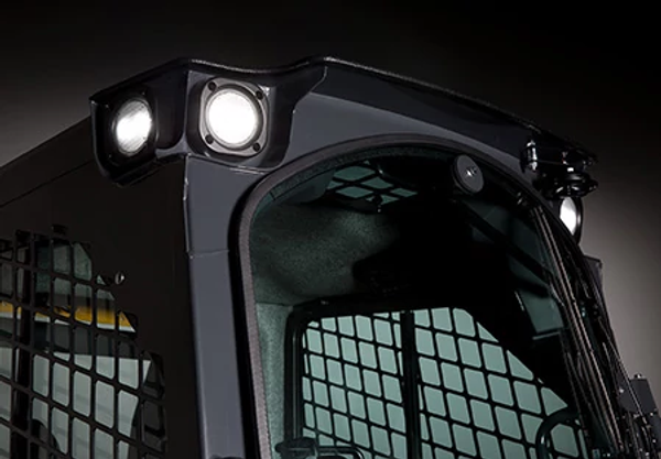 Close-up of the upper cab of a compact loader, showing bright LED work lights mounted on the roof and protective metal mesh around the cab