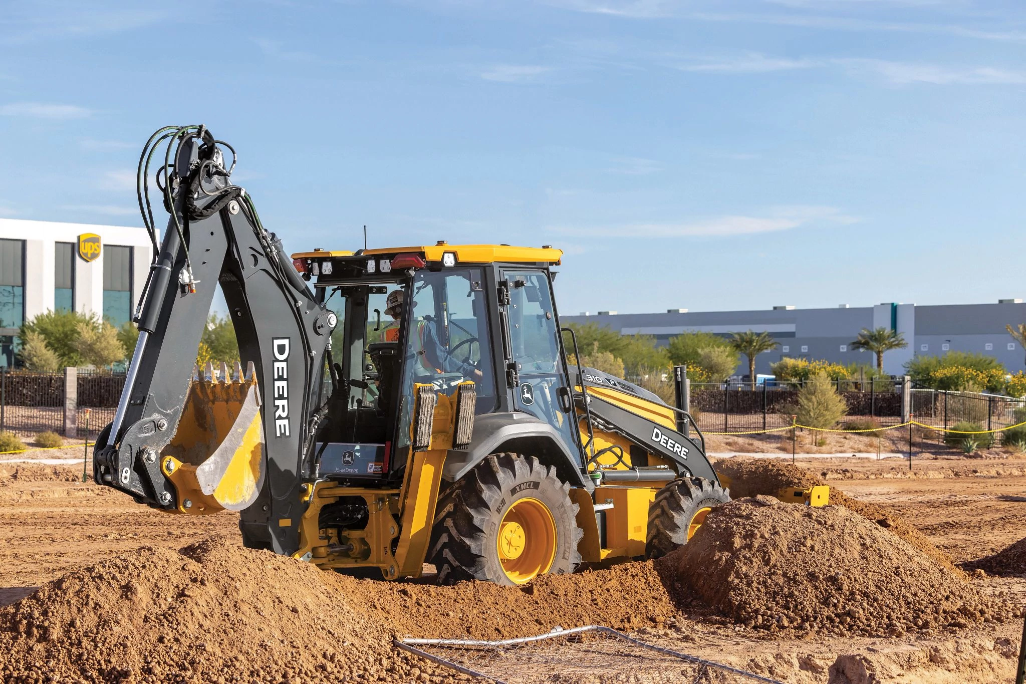310 P-Tier Backhoe Loader excavating a dirt pile at a construction site