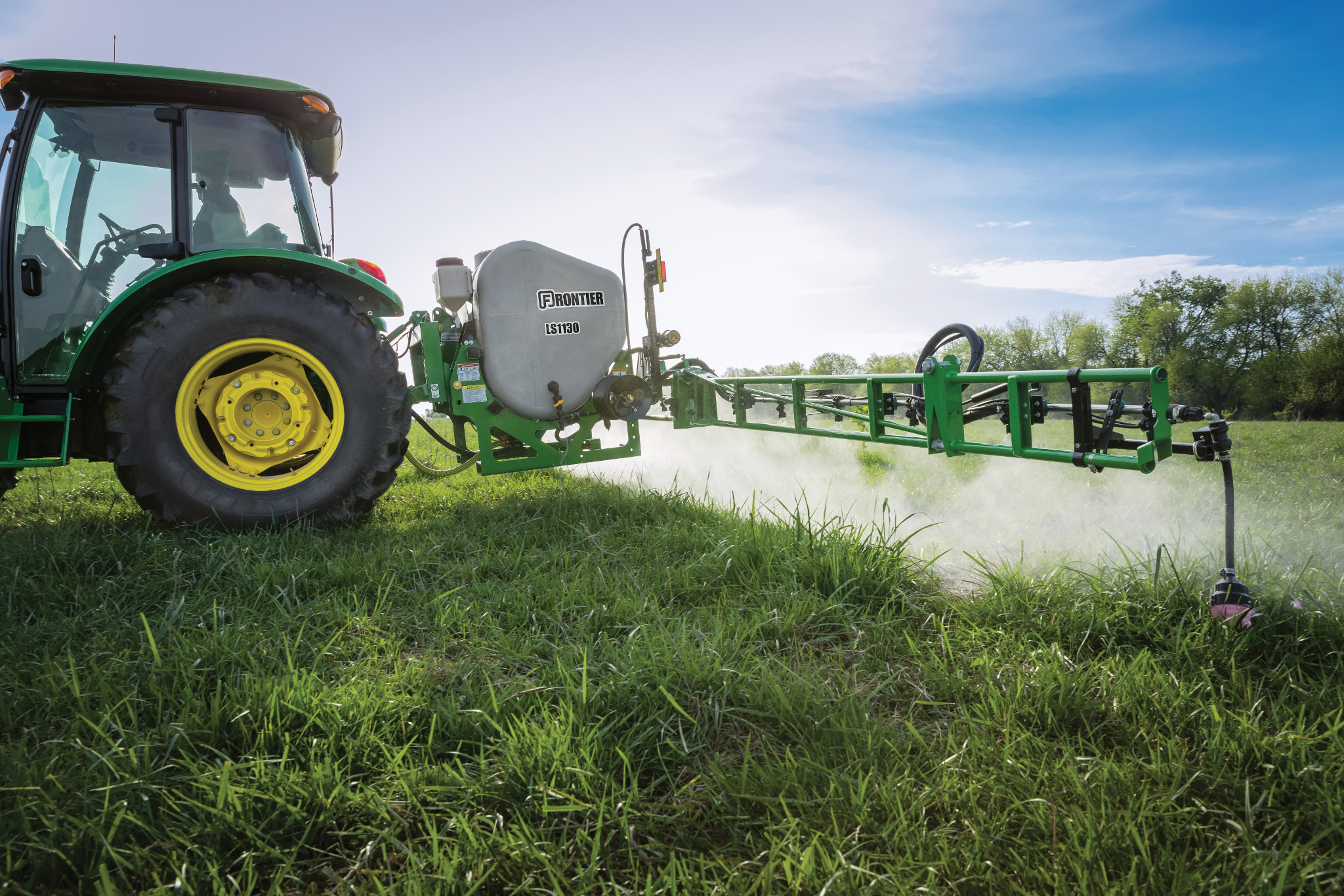 Field view of LS1130 Sprayer on 5075E Tractor spraying in grassy field