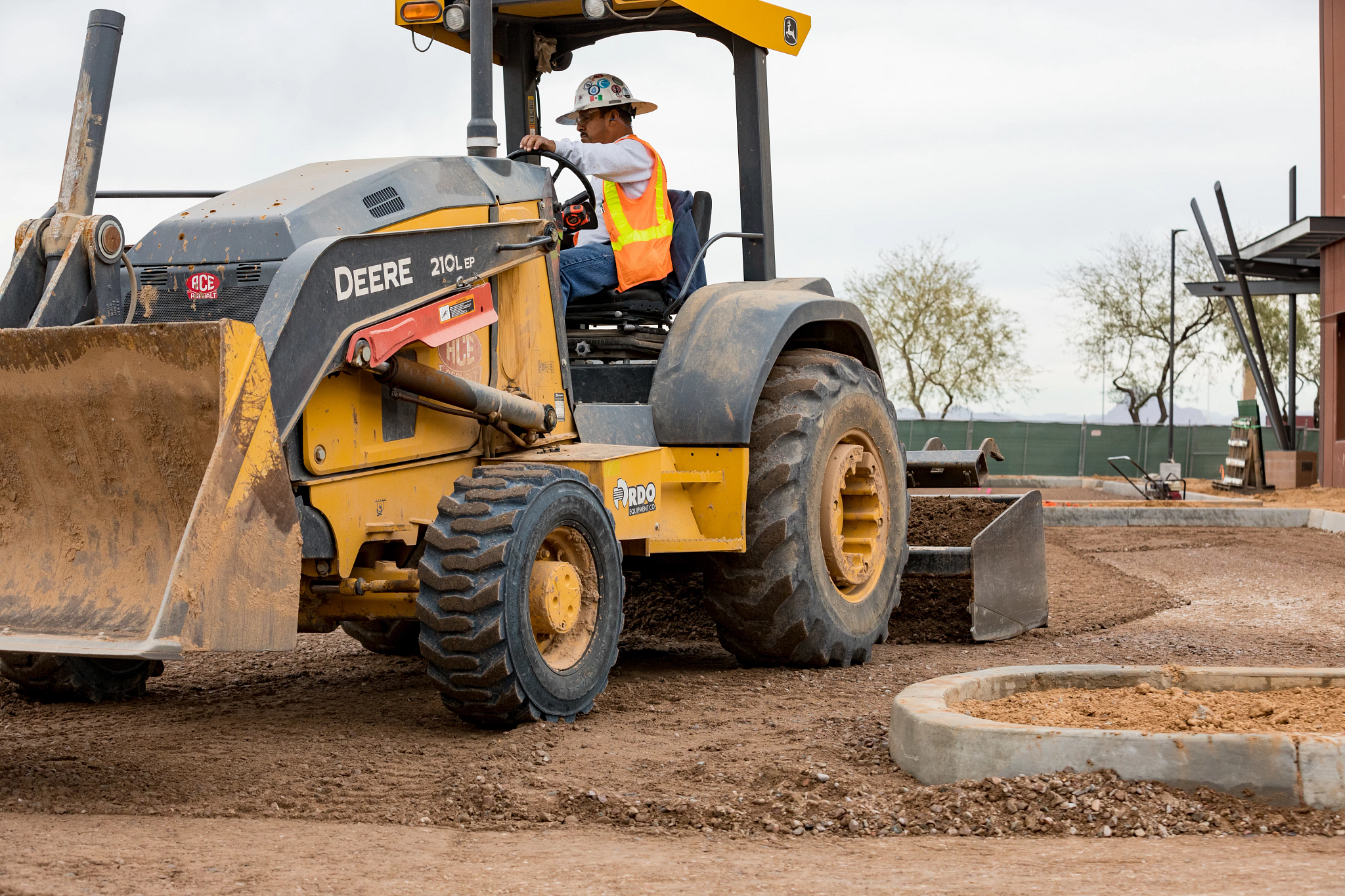 Front left view of a 210L EP Tractor Loader with BB84 box blade grading on a jobsite