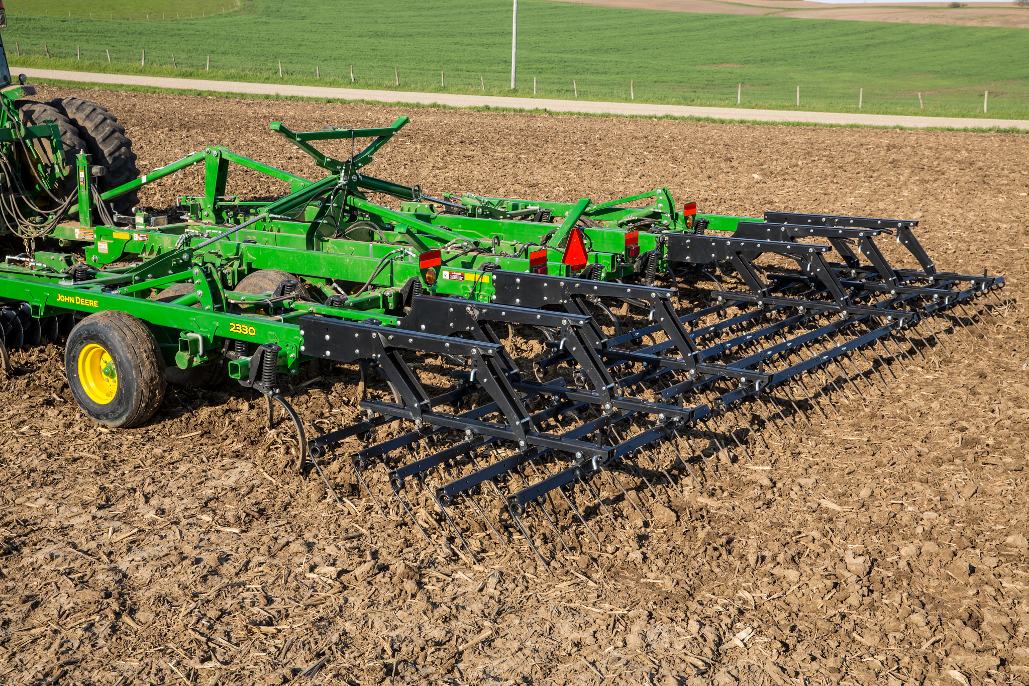 Field cultivator with spring-tooth tines working tilled soil in a farm field.