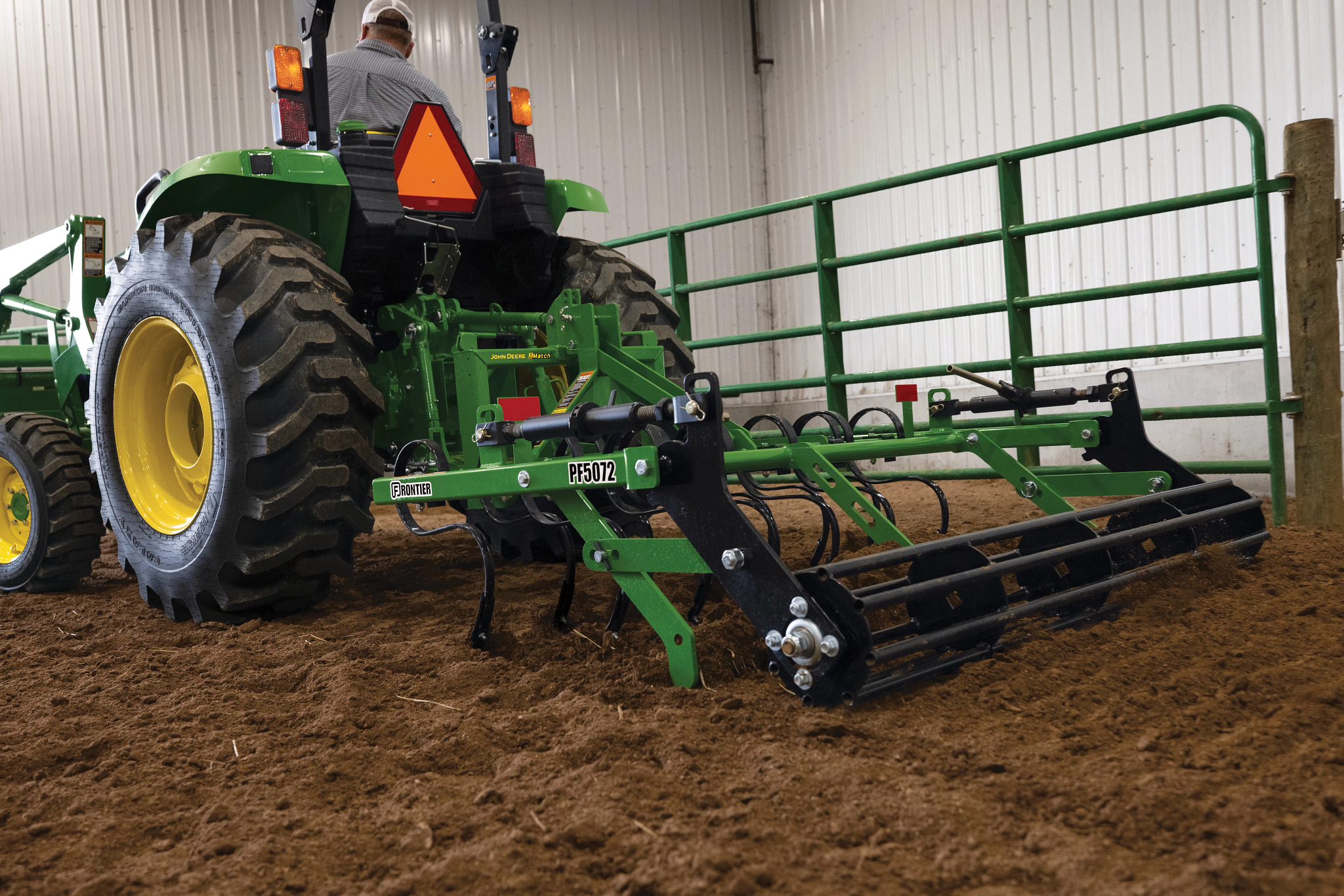 Rear left view of a tractor pulling a PF5072 Pro Finisher across an indoor riding arena