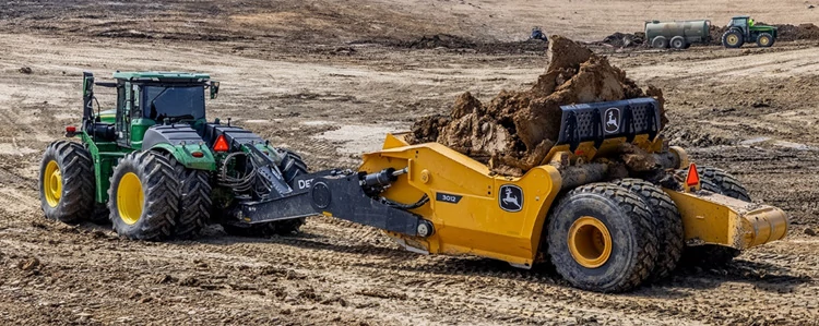 Side left view of a 9 series tractor pulling a loaded 3012 4-Tire Ejector Scraper across a dirt lot