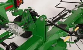 Close-up of a green tedder implement showing pivoting linkage arms, hydraulic lines, fittings, and mounting hardware