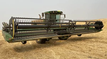 A wide draper platform attached to a self‑propelled windrower, viewed from a front angle while positioned in a cut wheat field