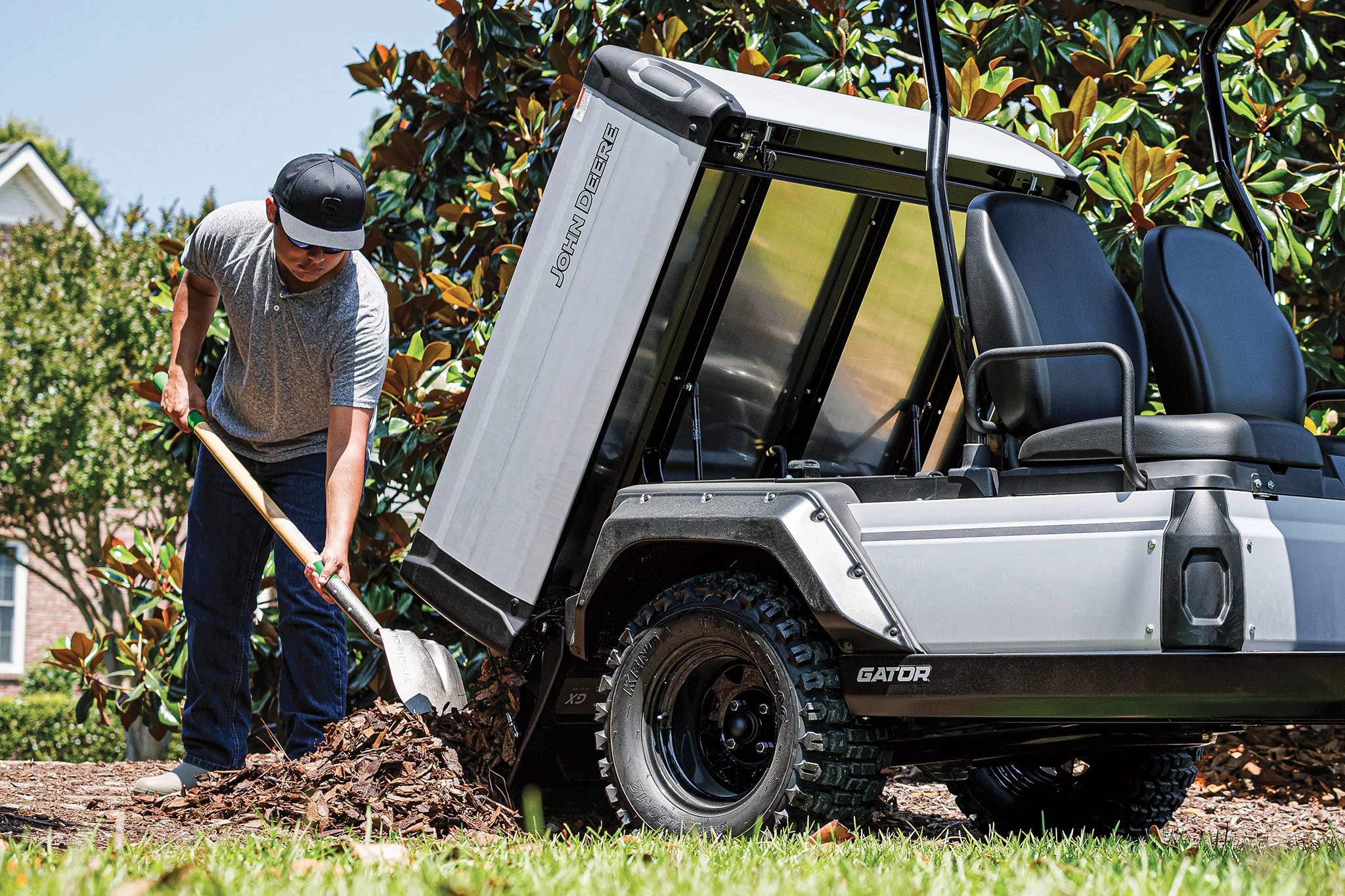 Close-up, side right view of the extended cargo box of a metallic grey Gator GX with landscaper shoveling woodchips behind it