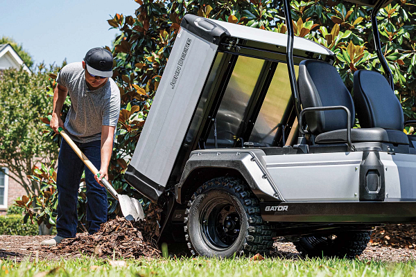 Close-up, side right view of the extended cargo box of a metallic grey Gator GX with landscaper shoveling woodchips behind it