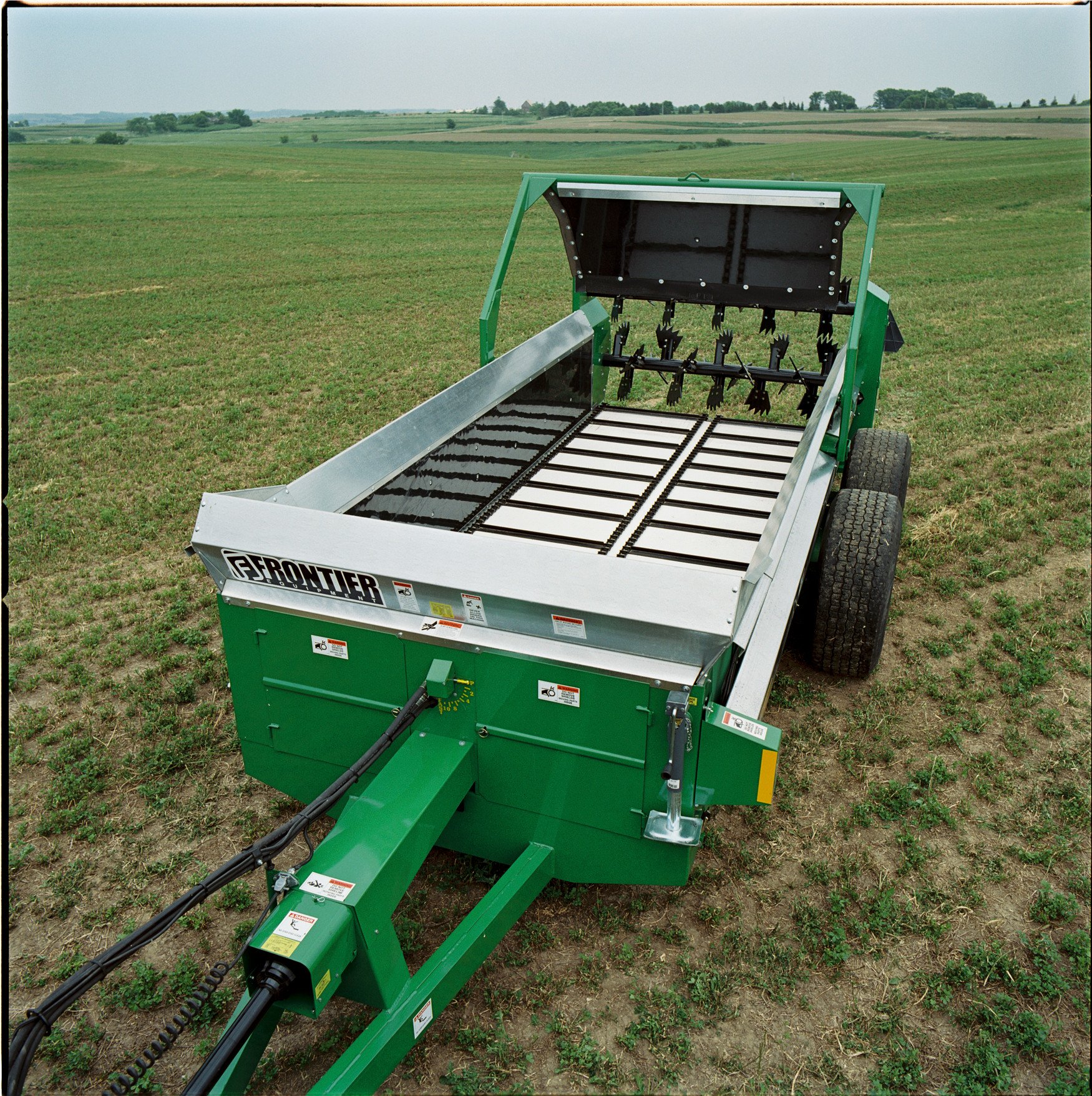 Front left overhead view of galvanized steel spreader box on MS12 Manure Spreader in a large open field