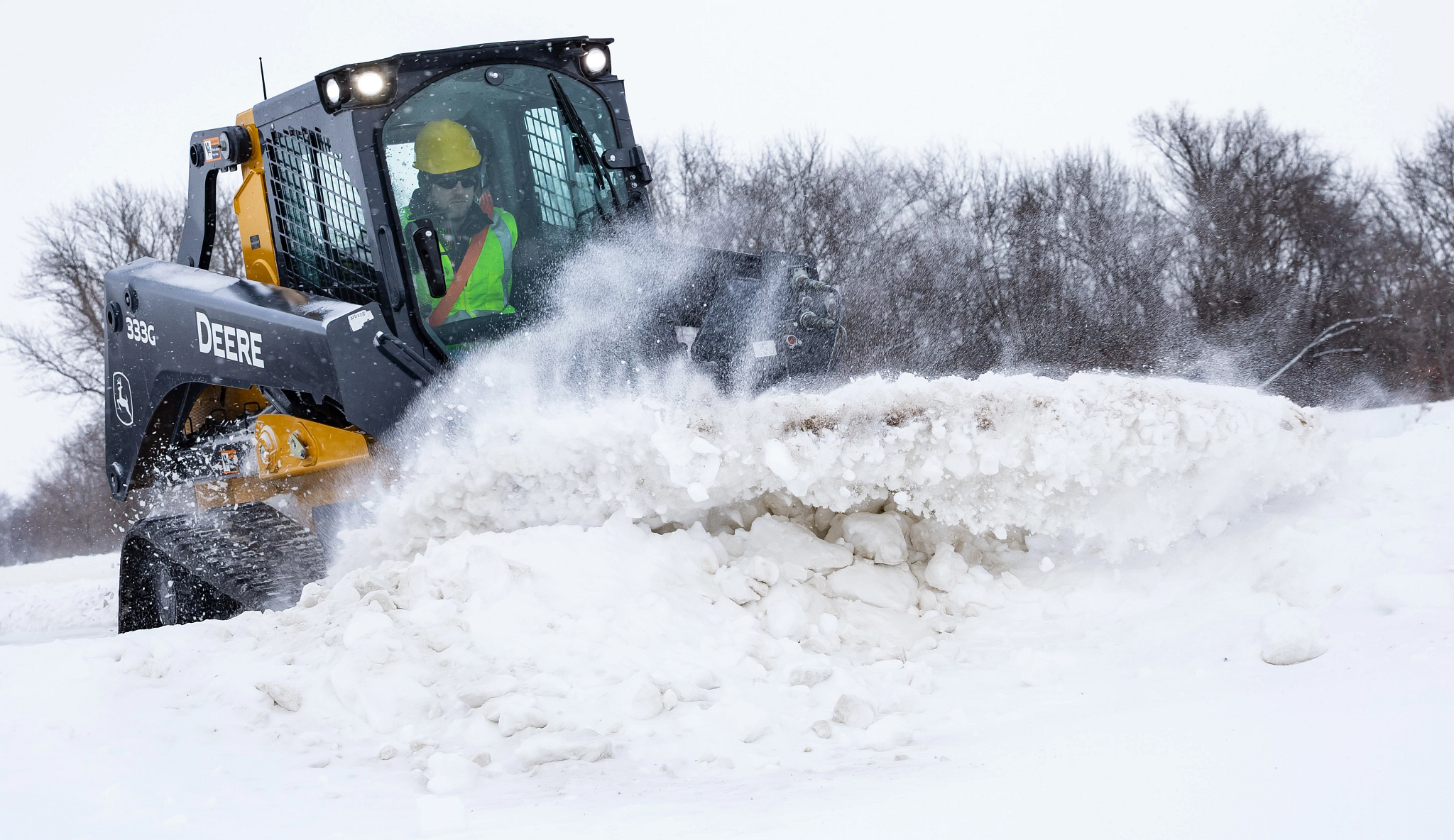 Front right view of a 333G compact track loader pushing a snow bank up with BL9B Snow/Utility Blade
