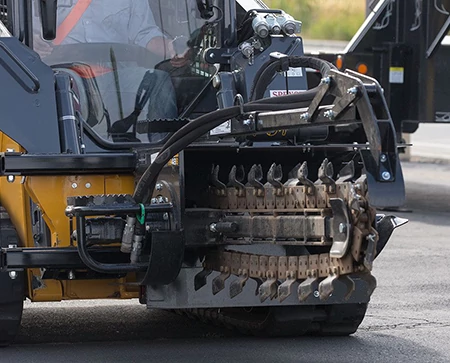 Front view of a TR series trencher attached to a loader traveling down a street