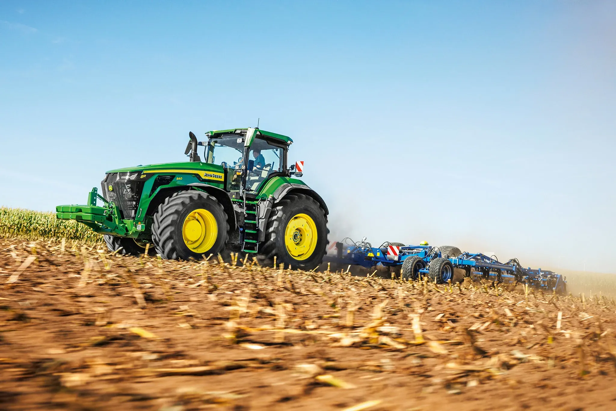 Tracteur 8R 540 tirant un outil de travail du sol dans un champ de maïs coupé