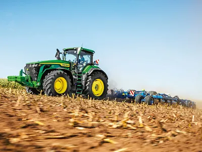 Tracteur 8R 540 tirant un outil de travail du sol dans un champ de maïs coupé