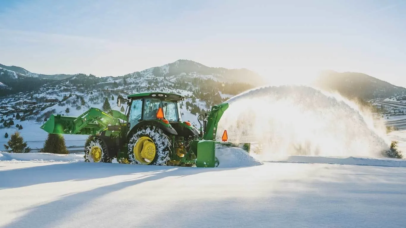 SB13 Snowblower attached to a tractor blowing snow in front of a mountain