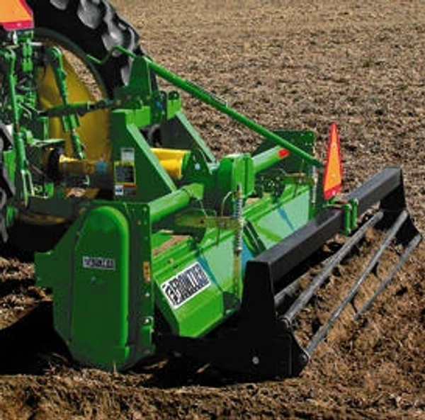 Green Frontier soil‑conditioning or seedbed‑preparation attachment mounted behind a tractor, showing the rear leveling bar and guard with an orange safety slow‑moving vehicle sign visible above the implement.