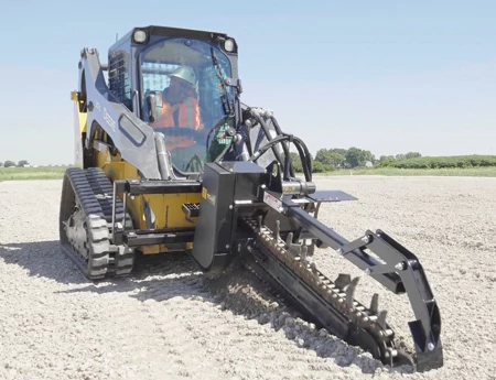 Front view of a TC48 trencher barreling into gravel on the front of a compact track loader