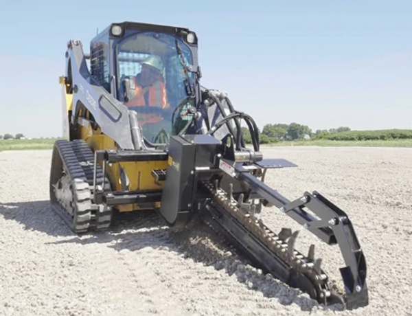 Front view of a TC48 trencher barreling into gravel on the front of a compact track loader