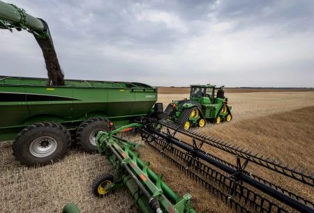 S Series Combine with Hinged Draper header unloading on-the-go in a field into a tractor's pull-behind grain cart
