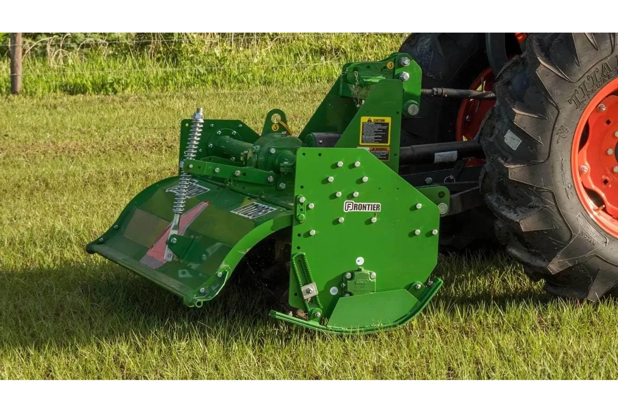 Right side view of RT12 Series Rotary Tiller pulled by a tractor through a grassy field