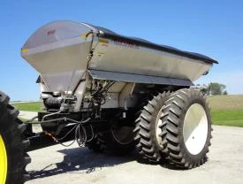 Front left view of a silver pull-type dry box spreader with two product bins resting in a yard.