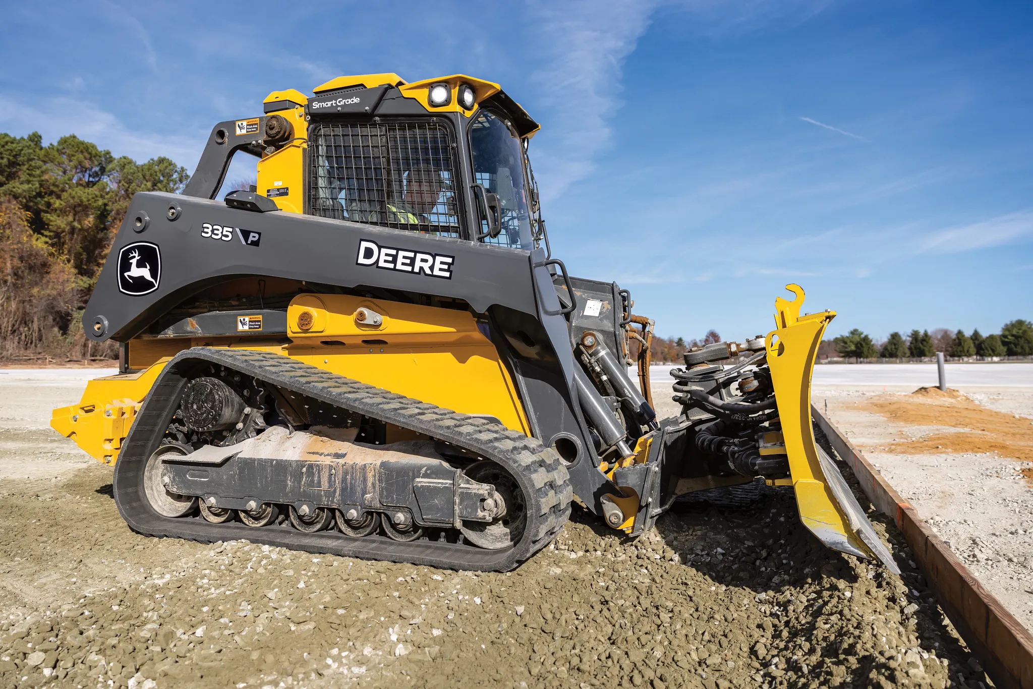 Side right view of a 335 P-Tier Compact Track Loader pushing gravel and forms into place on a jobsite