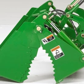 Close-up of a green hydraulic 4-in-1 bucket attachment with serrated metal jaws, hydraulic hoses, and warning labels
