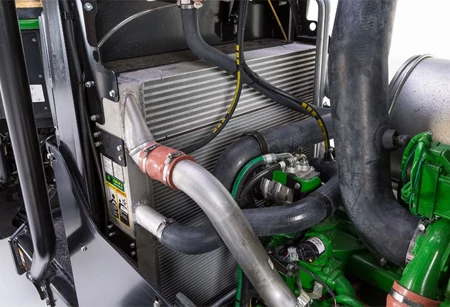 Close-up of a wheeled harvester's stacked cooling system, showing pipes, cables, and variable-speed reversing fan