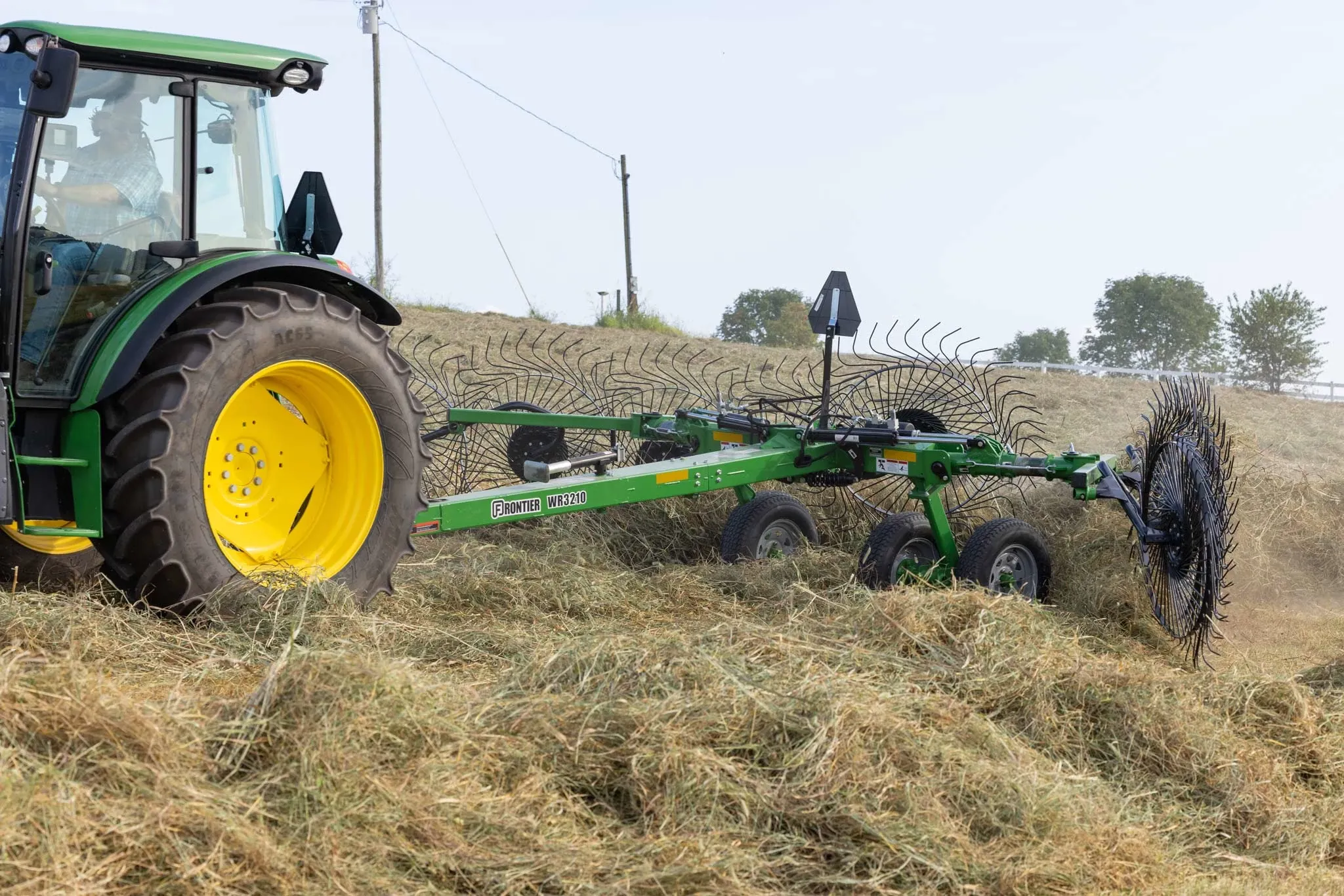 Side left closeup of a 5125M tractor pulling a WR3210 wheel rake through thick felled hay