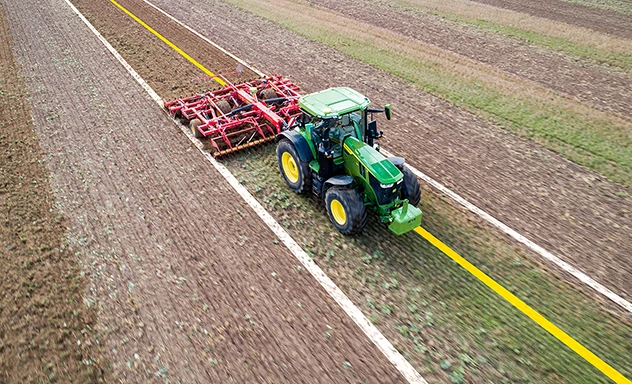 Photo of tractor pulling an implement in a field with AutoTrac Implement Guidance lines projected onto it