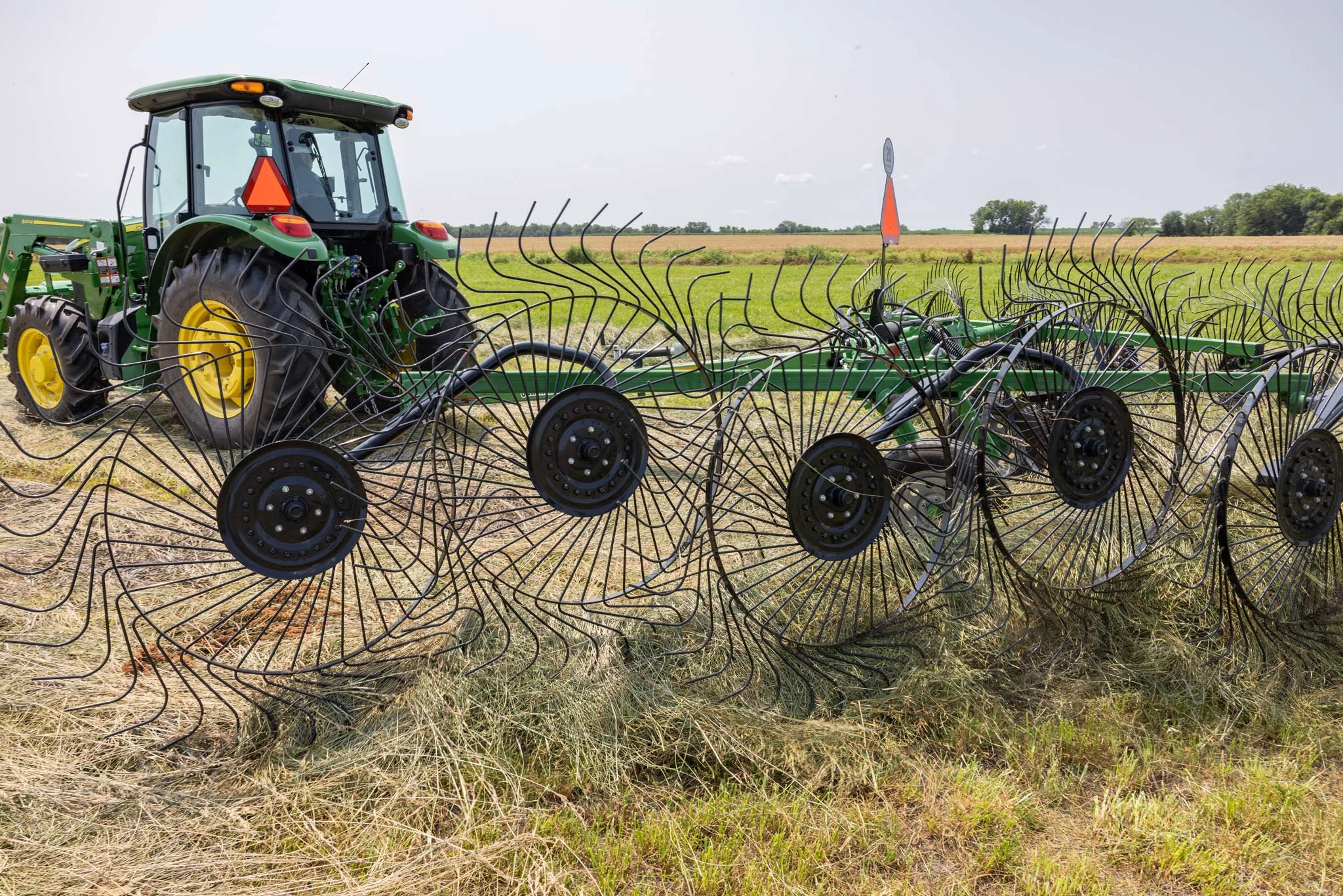 Side left view of a WR3212 wheel rake on hay with attached 5E tractor in the background