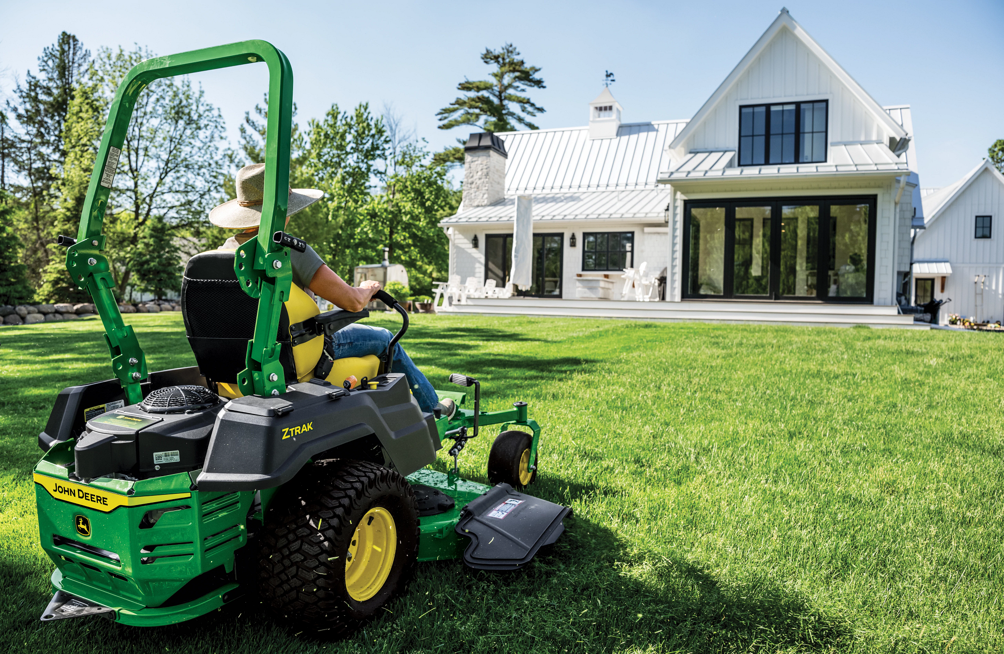 A rear-right-facing view of a green zero-turn mower and its engine as it mows the lawn of a residence.