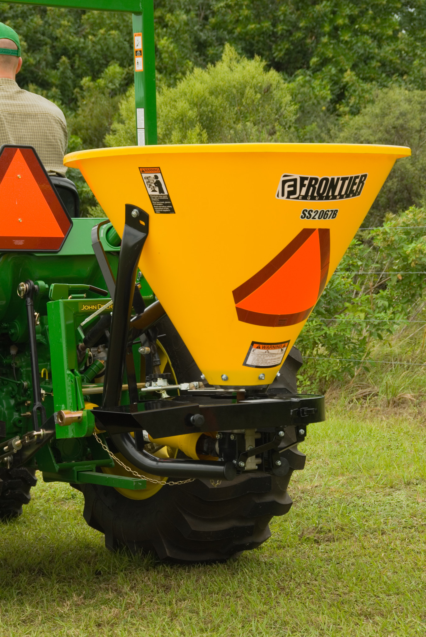 Rear left view of SS20B Broadcast Spreader with polyethylene hopper mounted on a tractor driving in a field