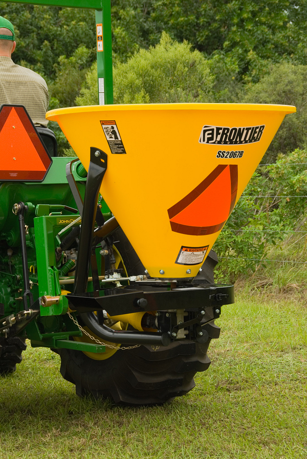 Rear left view of SS20B Broadcast Spreader with polyethylene hopper mounted on a tractor driving in a field