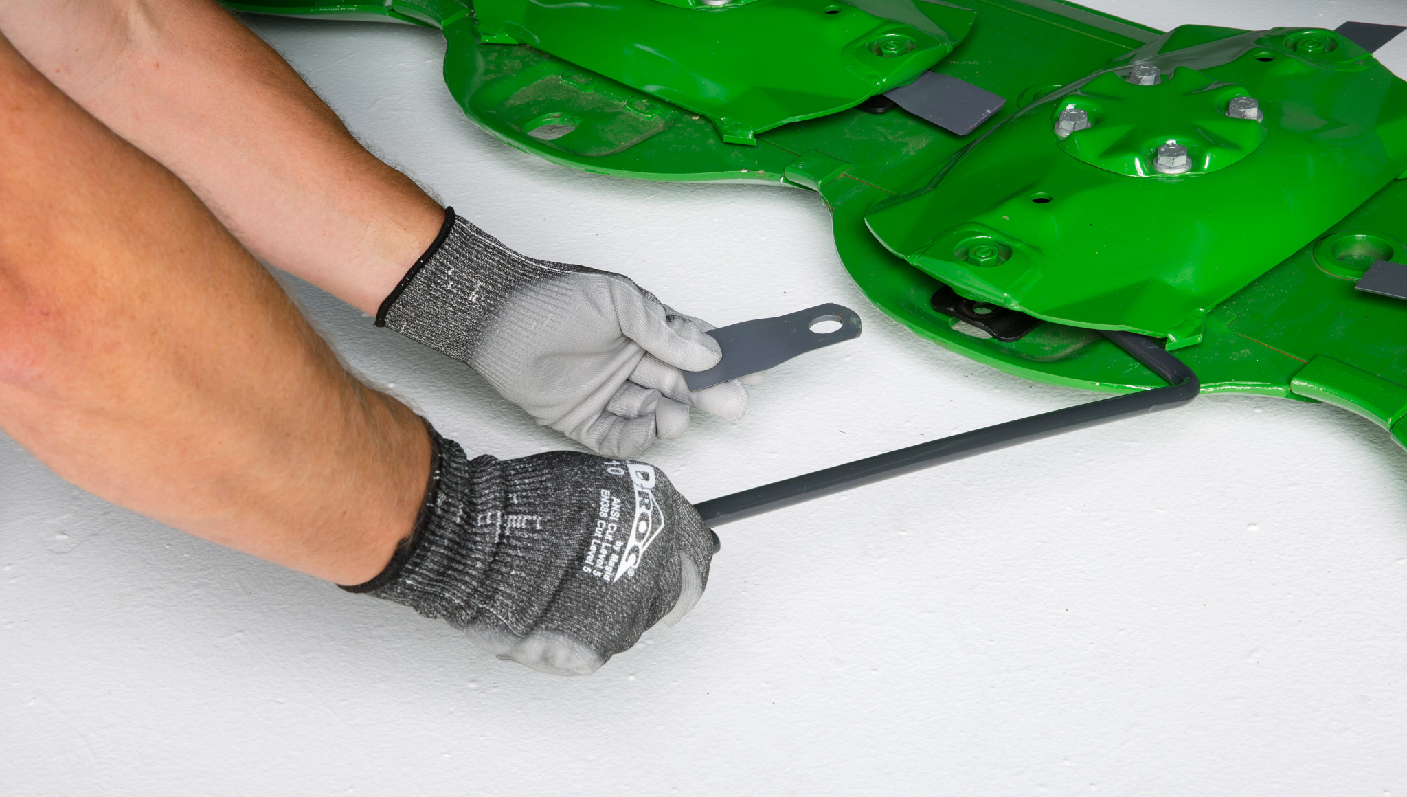 Mechanic's arms demonstrating quick-change knives technology with two tools on a R990R Rear Mount Mower-Conditioner's cutterbar