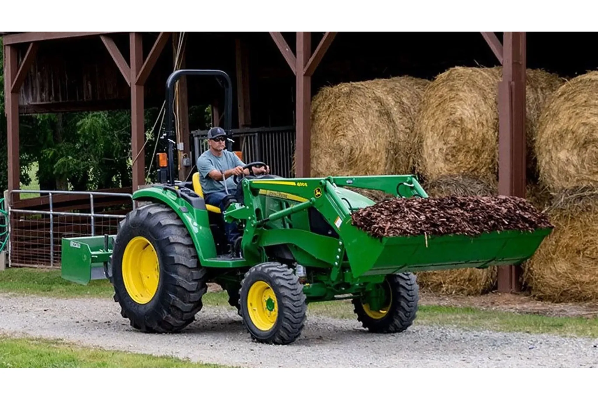 farmer operating a 4044M Compact Tractor to move mulch in front of hay bales