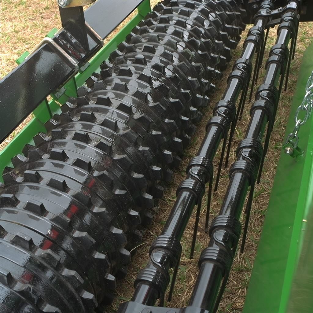 Close-up view of a rear cultipacker, showing a large black notched roller next to a series of black rotating tine bars mounted on a green frame