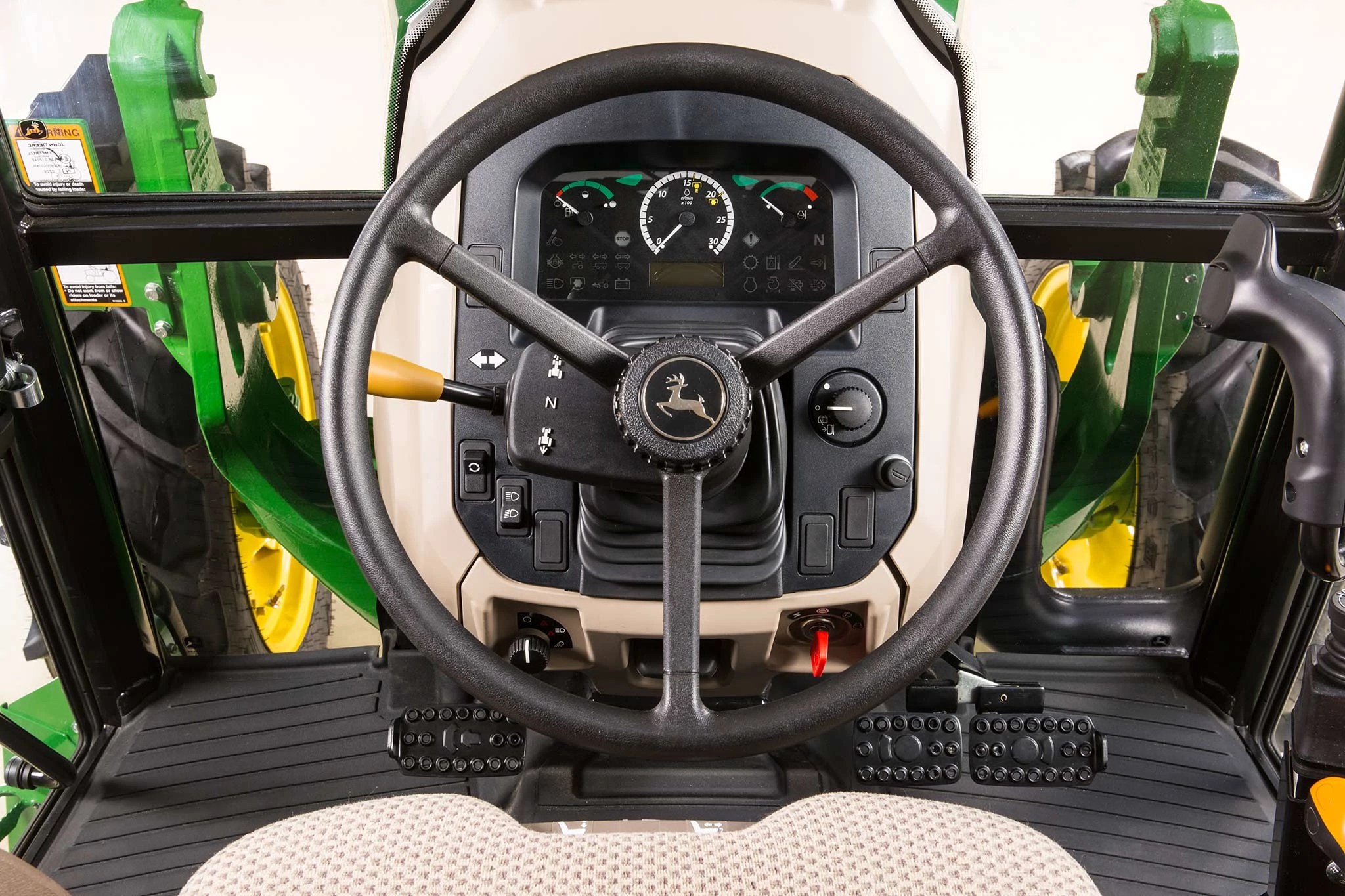 Front, studio, in-cab view of the steering wheel, pedals, and dash of a 5075E Cab tractor