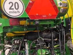 Close-up view of machinery with visible hoses and hydraulics, featuring an orange slow‑moving vehicle triangle and a “20 mile/h” sign.