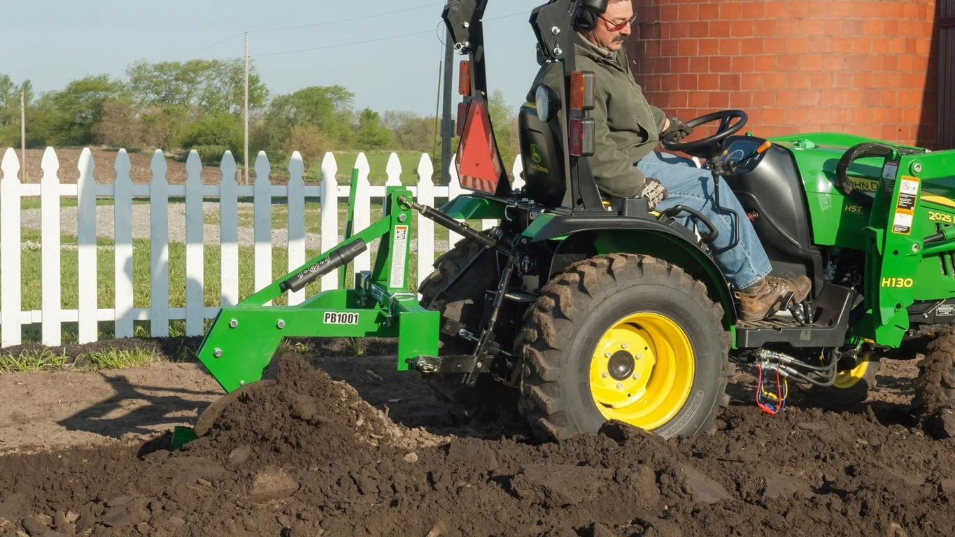 Frontier PB1001 Turning Plow tilling dirt in a small garden and being pulled by 3 Series Tractor