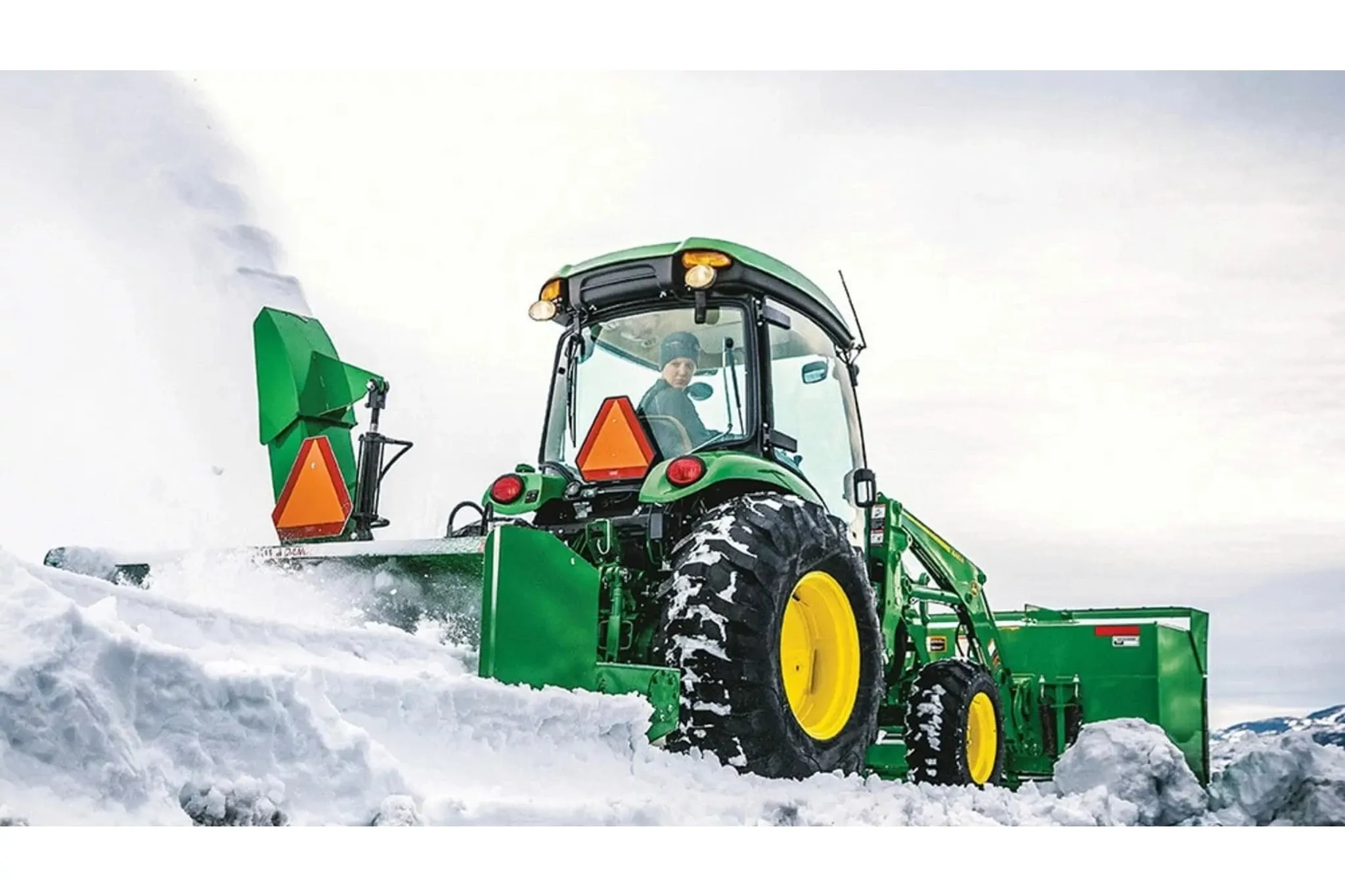 Person looking back as the snow removal attachment on a 4066r tractor throws snow.