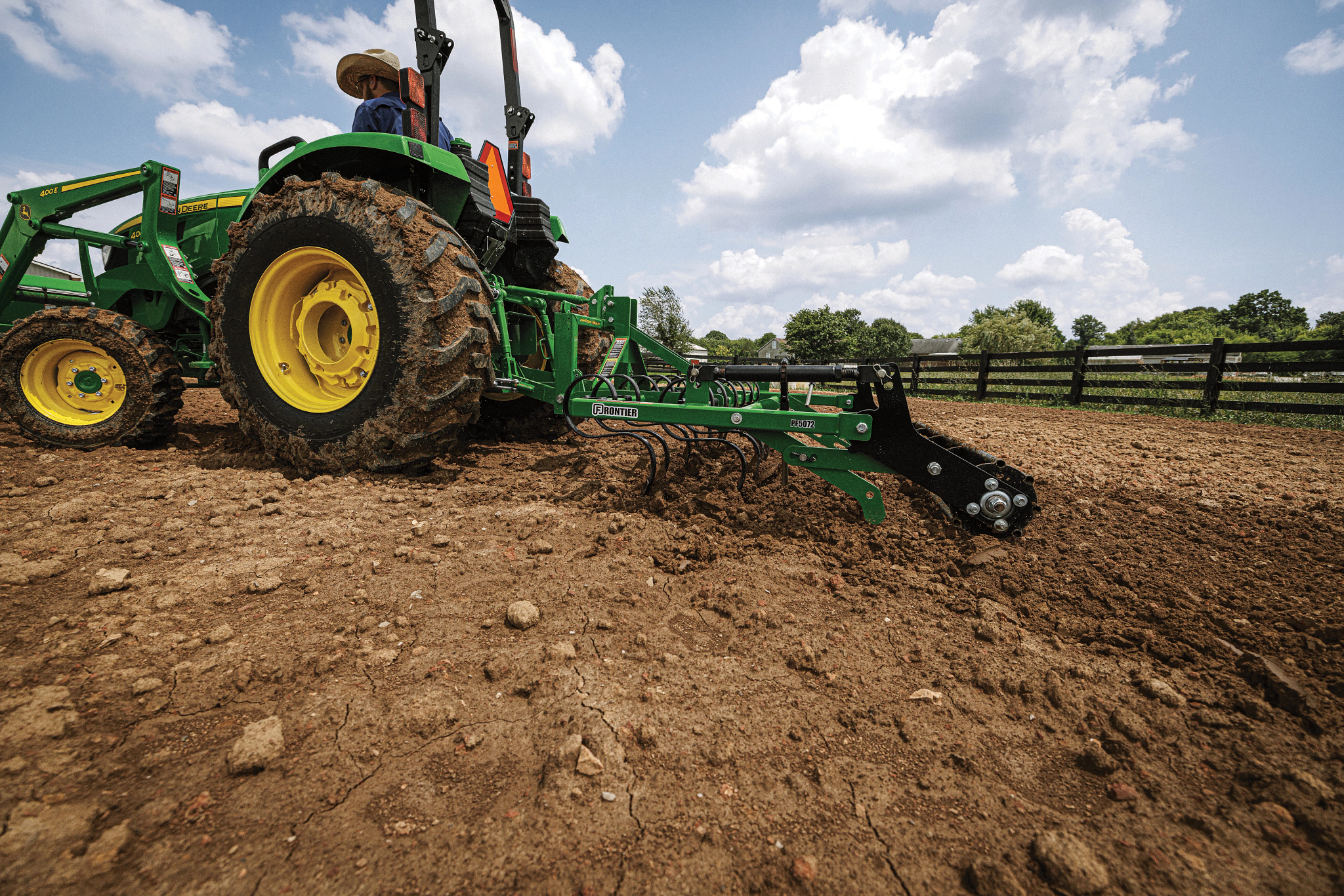 Side left view of a 4044M tractor with 400E loader dragging a PF5072 Pro Finisher across a fenced-in, dirt paddock