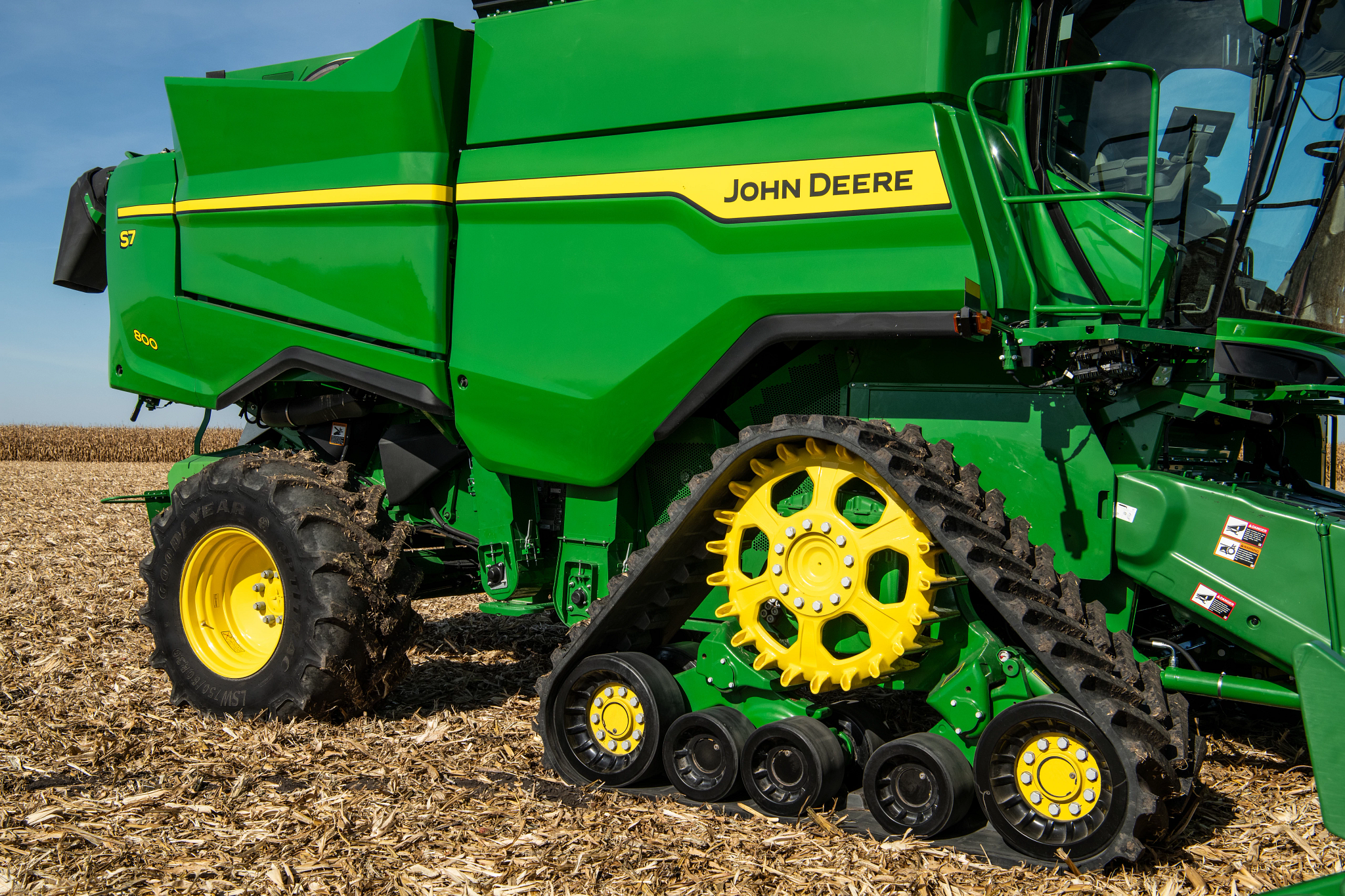 Side view of front track on an S7 900 Combine parked in a partially harvested corn field.
