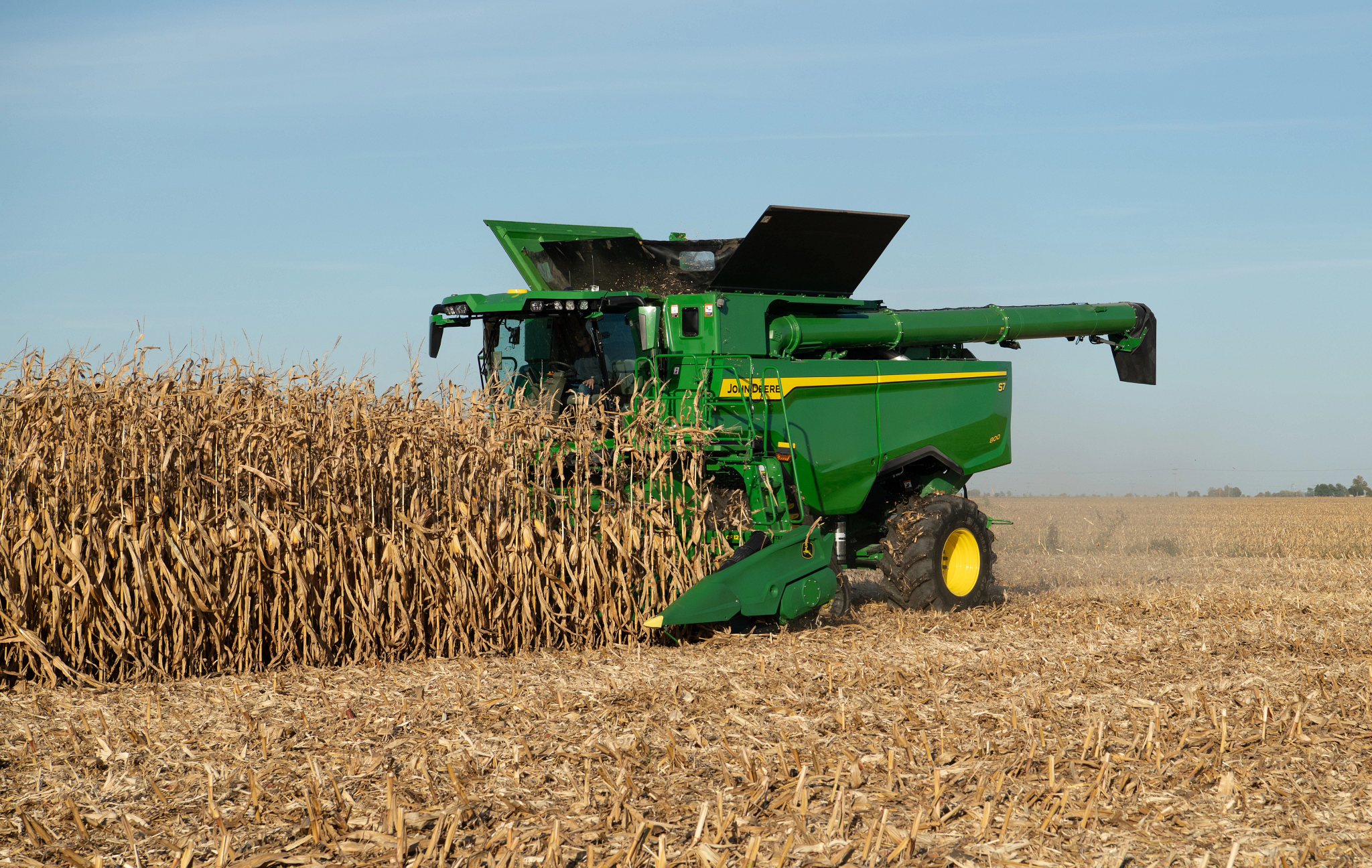 Front left view of an S7 800 combine harvesting corn in a field with attached CF12 folding corn head