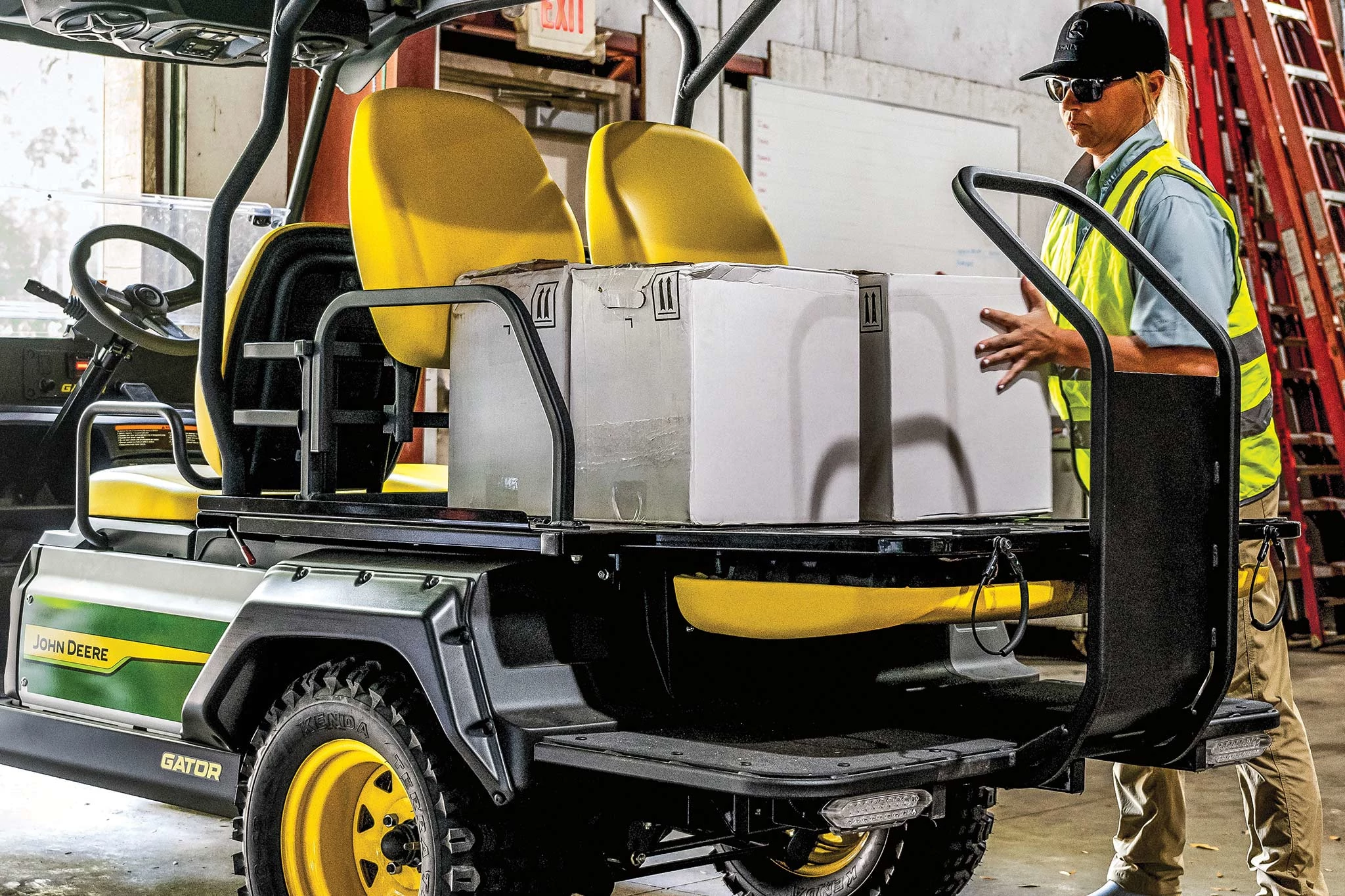 Rear left view of an Electric GX Crew Gator in a warehouse with worker loading boxes on top of the rear fold-down seats