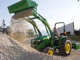 Side left view of an AY11H 4-in-1 bucket attached to tractor dumping gravel on a pile at full arm extension